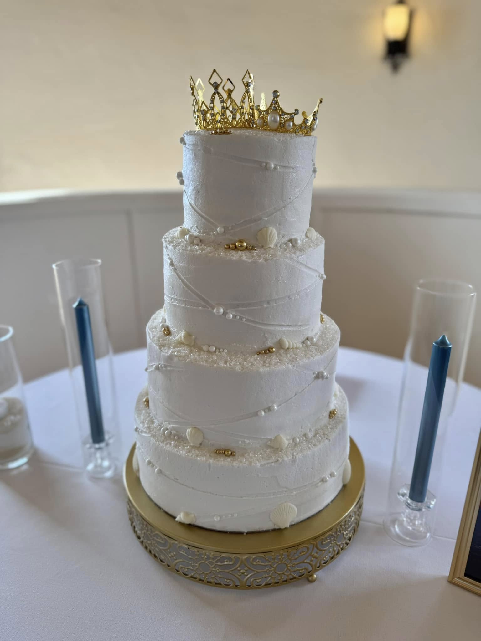 Four-tier white wedding cake with gold crown and pearl detailing
