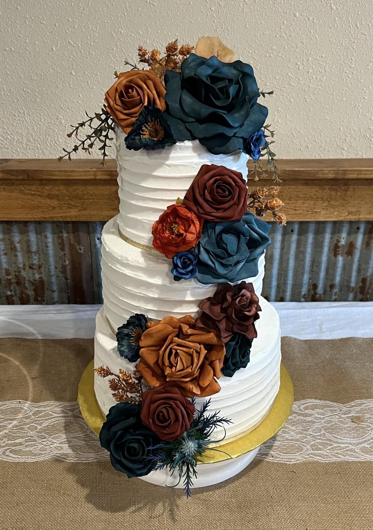 Three-tier white wedding cake with rust and navy floral cascade